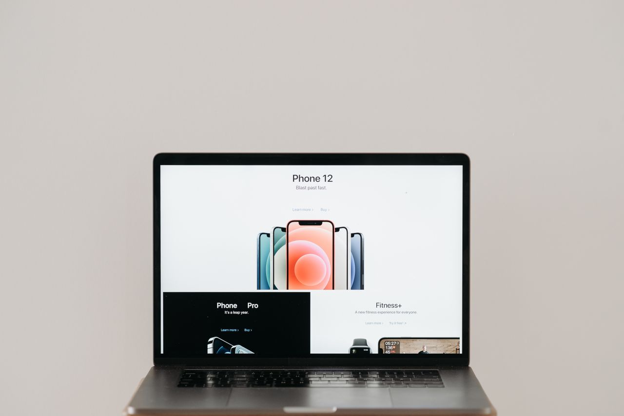 Laptop on stool showing sleek iPhone 12 ad, white background.